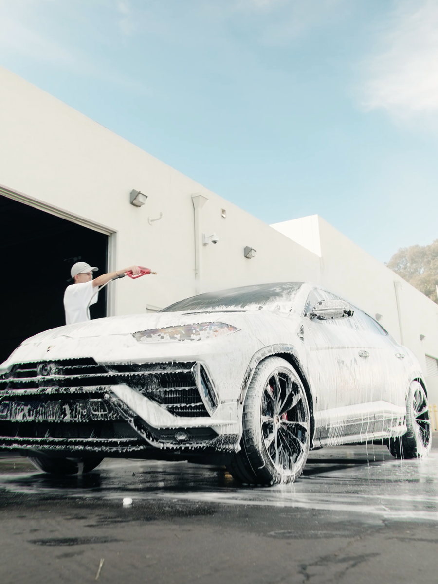 A vehicle covered in snow foam being rinsed outside a detail shop bay.